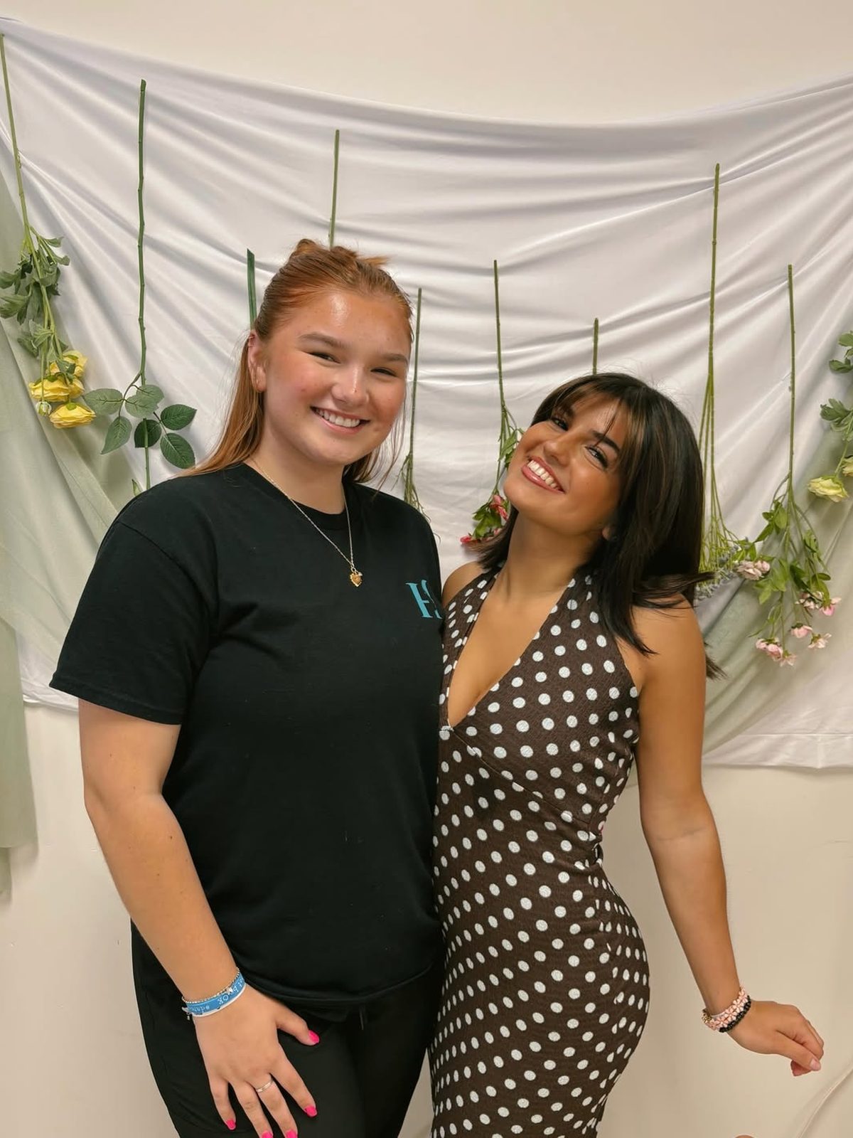 Myesa standing with a client in front of a white floral backdrop.
