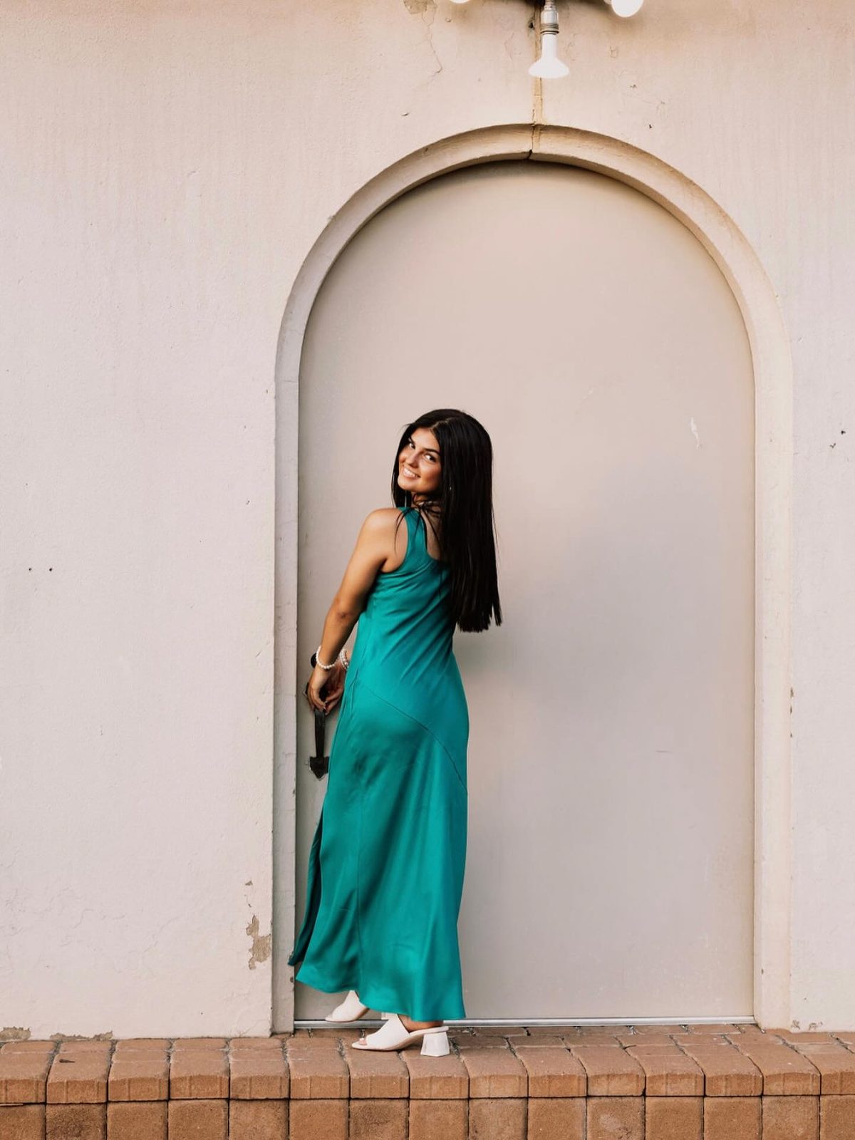 Myesa Camacho in a long teal dress, leaning against a cream archway.